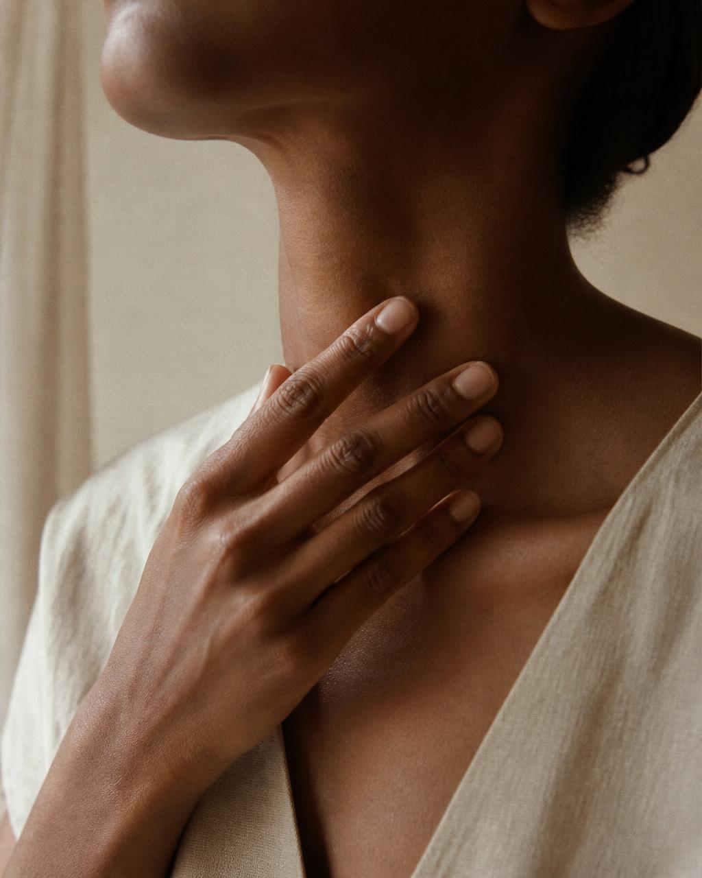 Close-up of a woman's hand resting at the base of her throat over the thyroid.